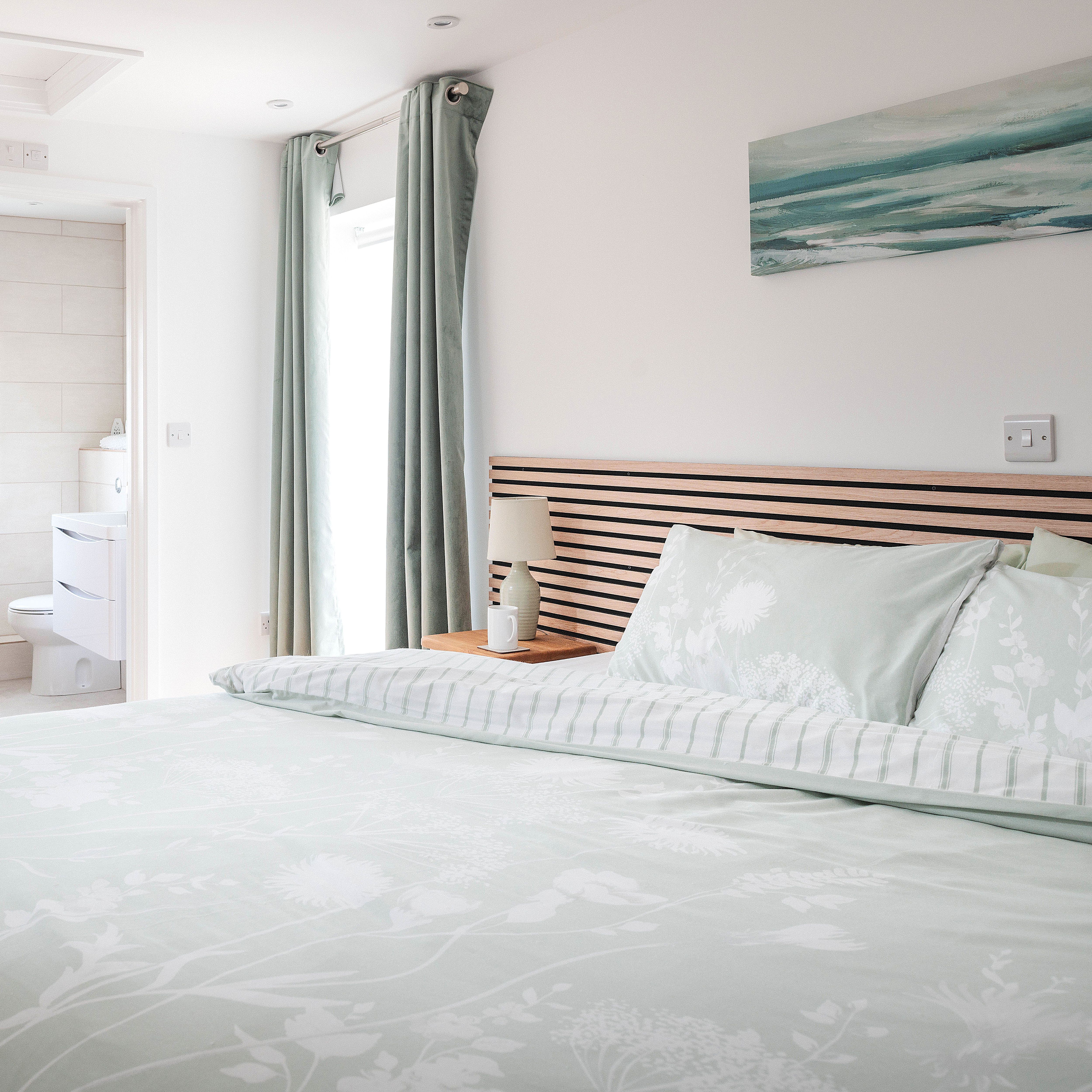 Modern bedroom with light pastel bedding and ensuite bathroom