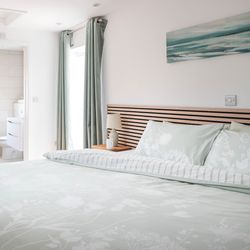 Modern bedroom with light pastel bedding and ensuite bathroom