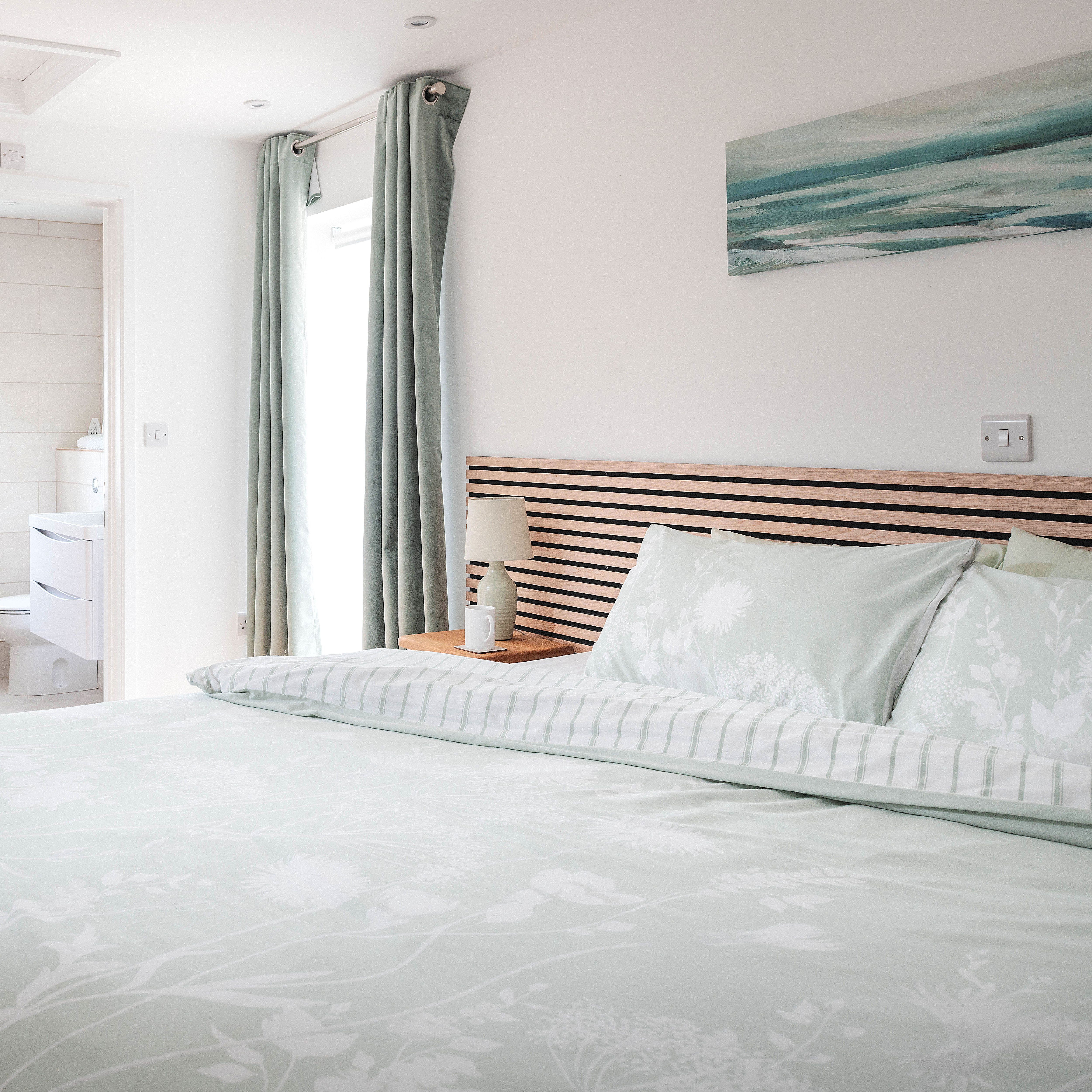 Modern bedroom with light pastel bedding and ensuite bathroom