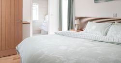 Modern bedroom with light pastel bedding and ensuite bathroom