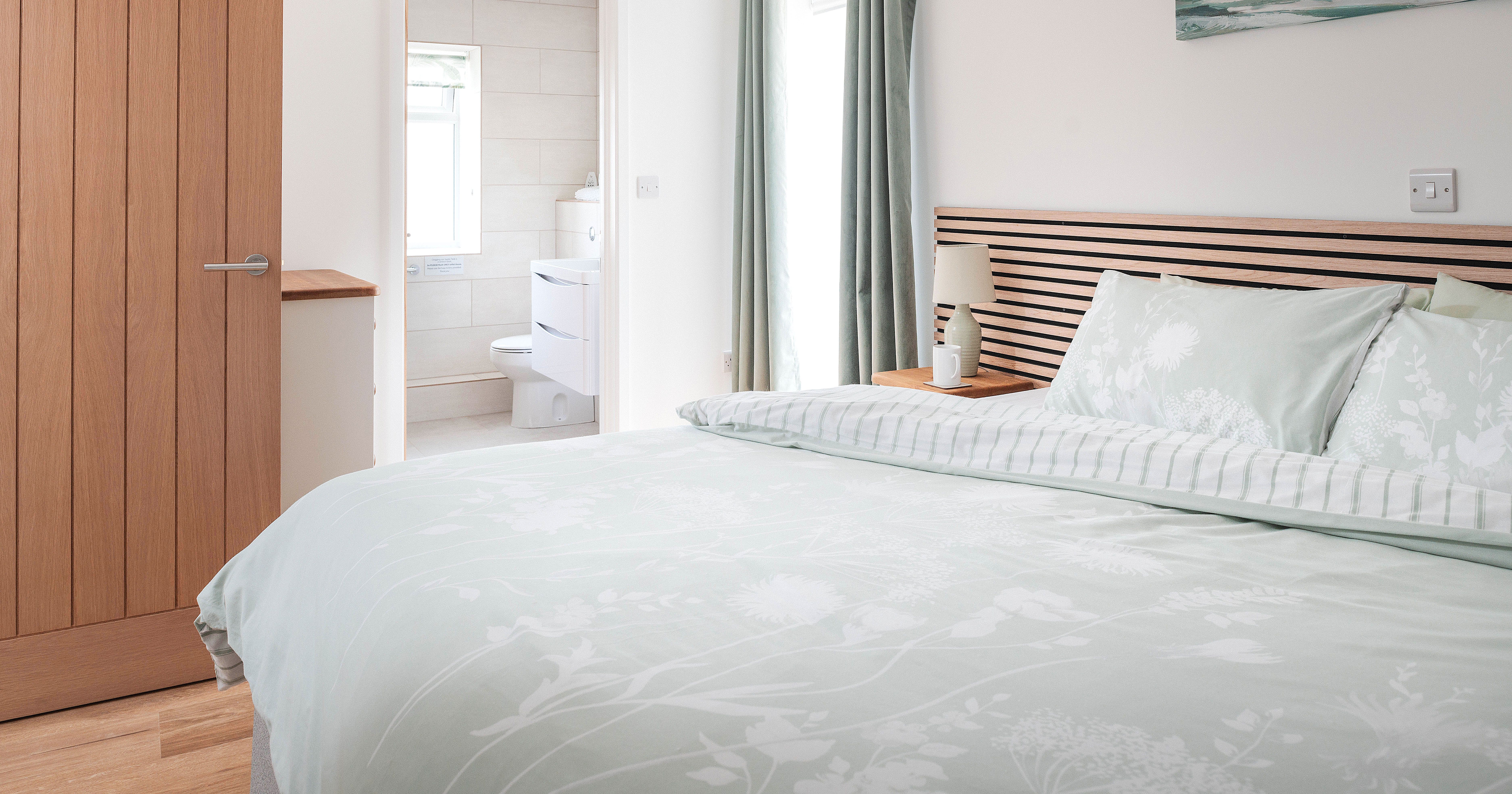 Modern bedroom with light pastel bedding and ensuite bathroom