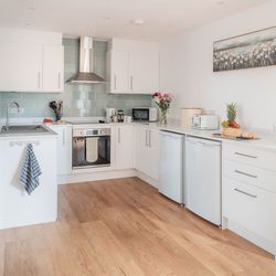 Modern white kitchen with wooden floors, stainless steel appliances, and fresh fruit on the counter.