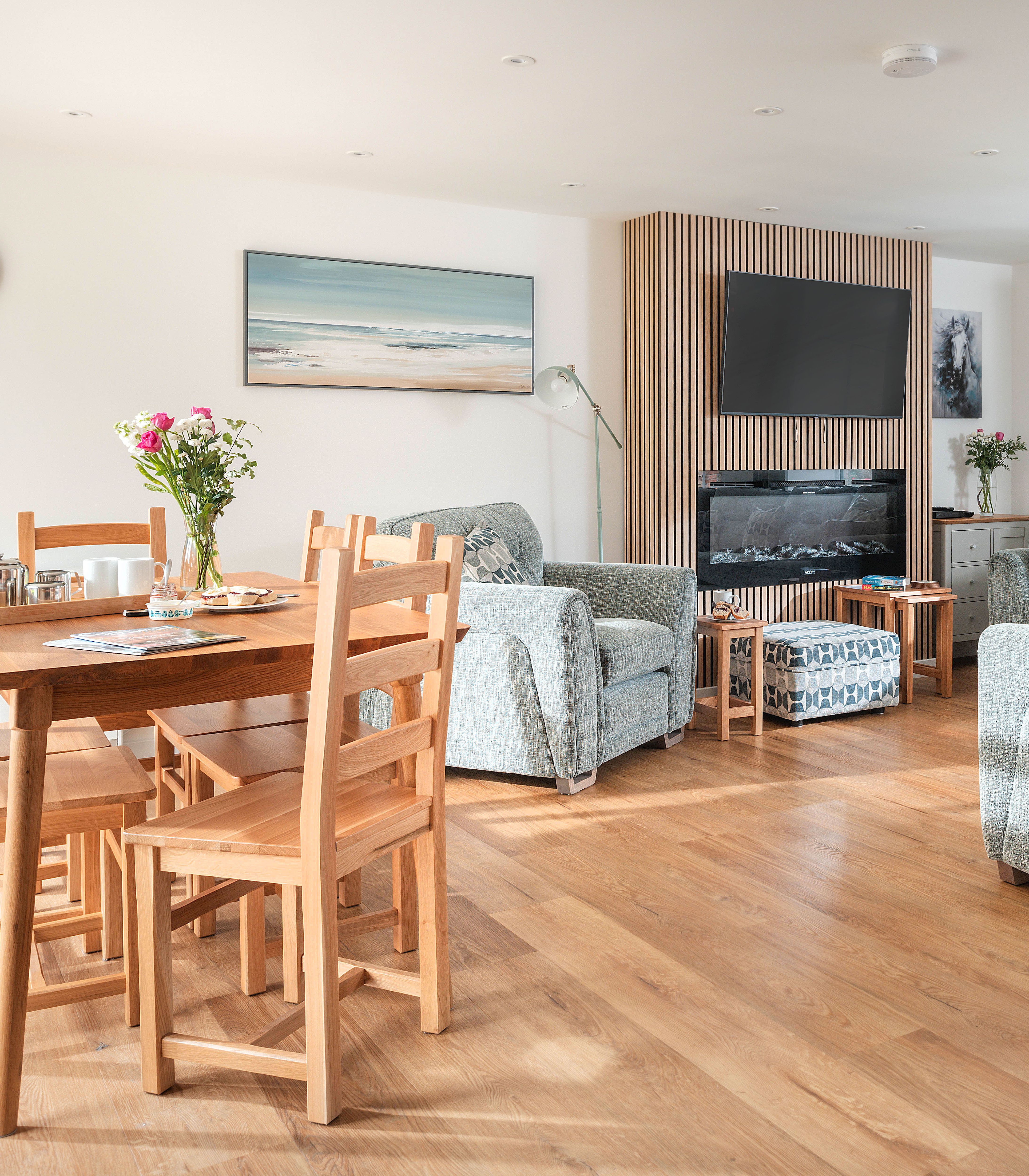 Modern lounge and dining area with grey sofas, wooden dining set, TV, and fireplace