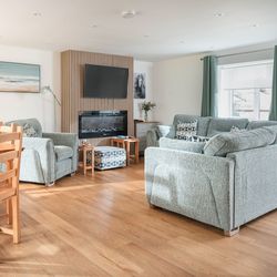 Modern lounge and dining area with grey sofas, wooden dining set, TV, and fireplace