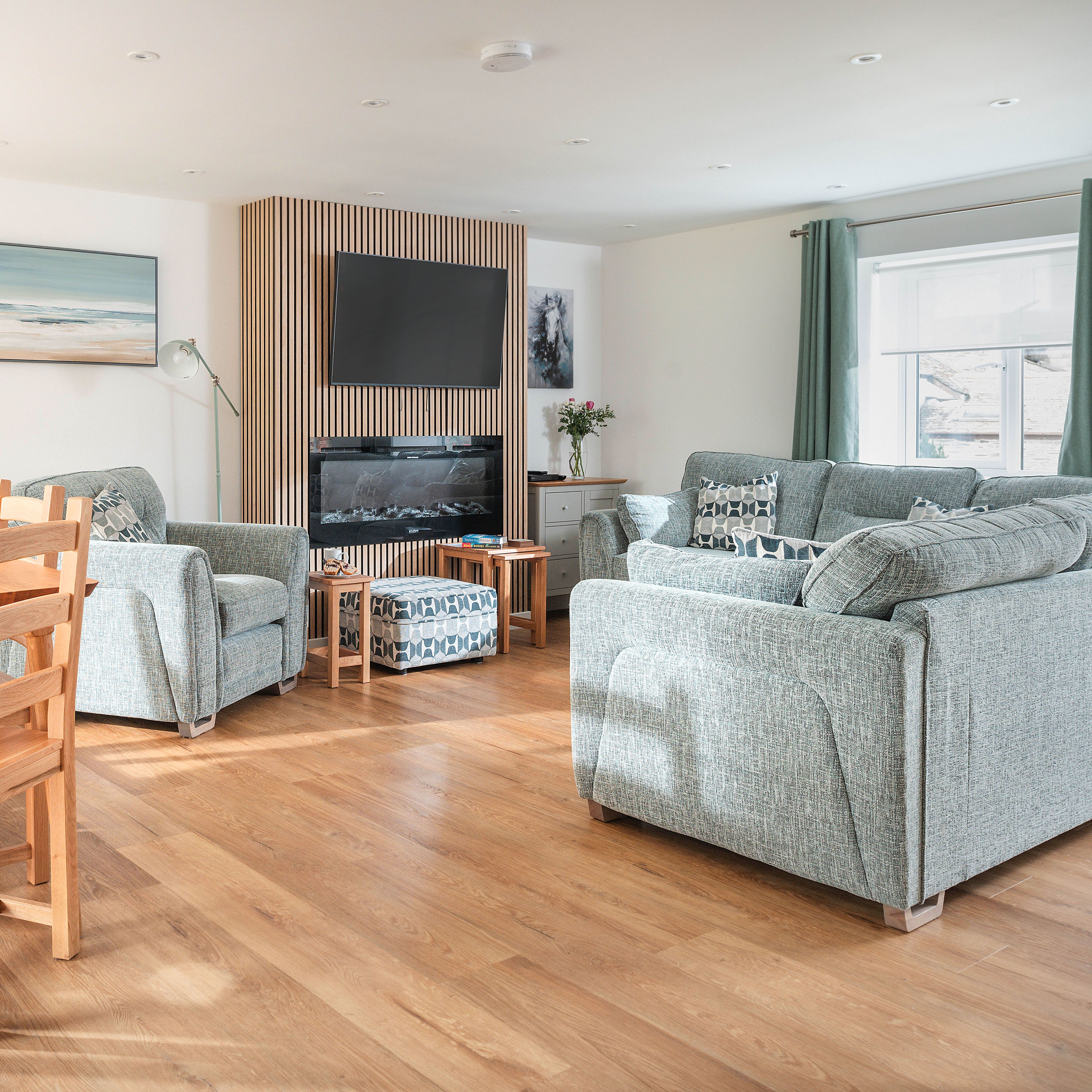 Modern lounge and dining area with grey sofas, wooden dining set, TV, and fireplace