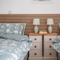 Two twin beds with green floral bedding, a wooden headboard, and a shared nightstand with lamps and books