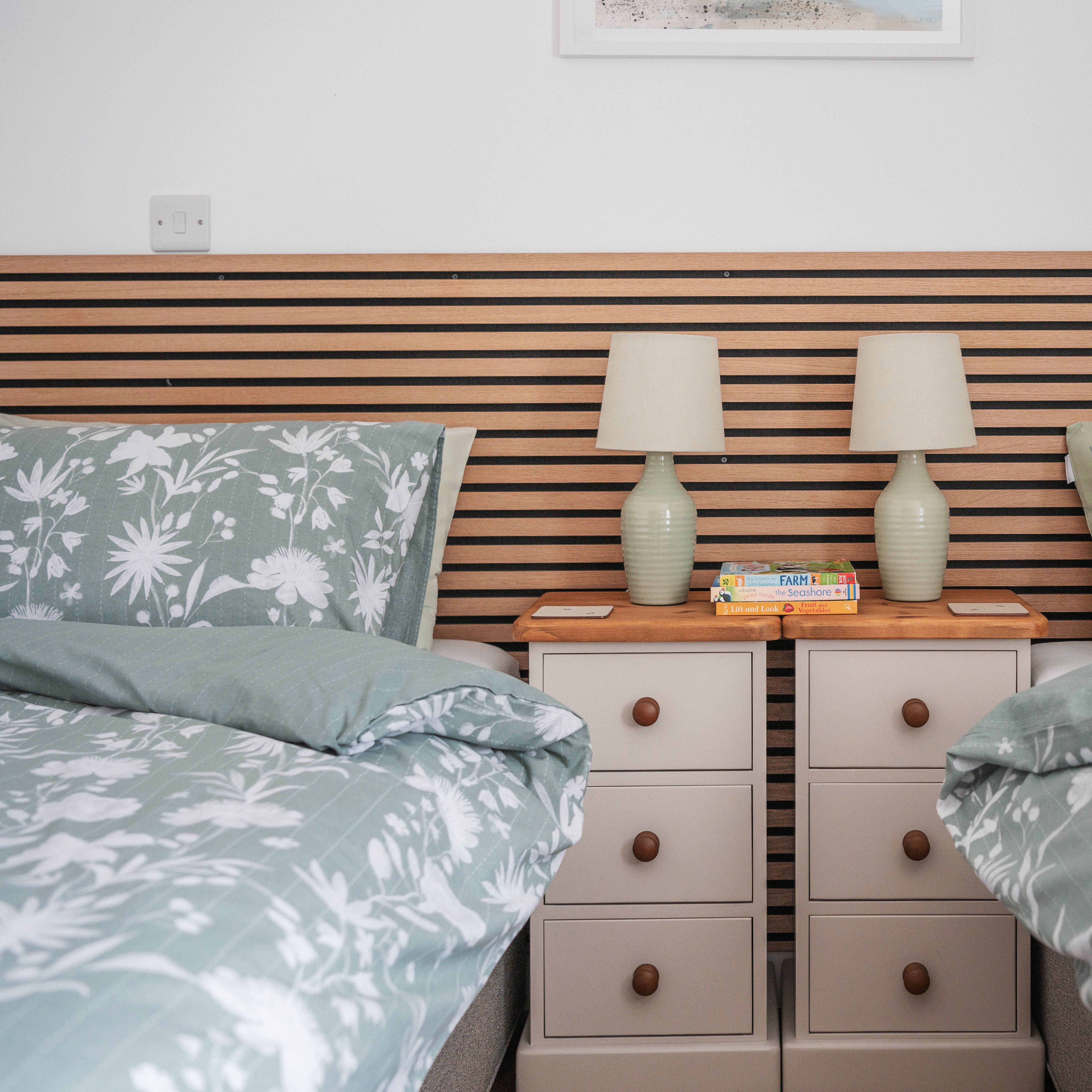 Two twin beds with green floral bedding, a wooden headboard, and a shared nightstand with lamps and books