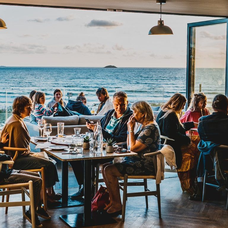 People dining at a restaurant with large windows overlooking the ocean.