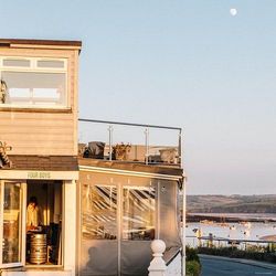 Cafe building overlooking a scenic waterfront with boats and hills in the background.