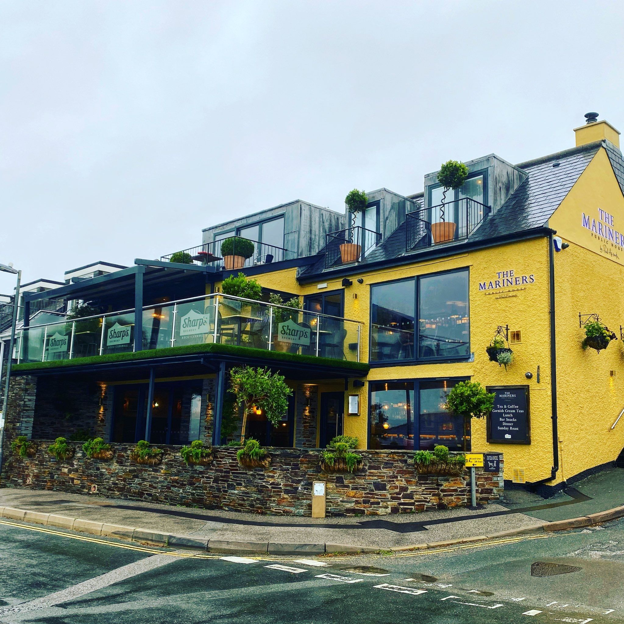 Exterior of The Mariners pub in Rock with yellow walls, glass terrace, and outdoor plants