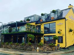 Exterior of The Mariners pub in Rock with yellow walls, glass terrace, and outdoor plants