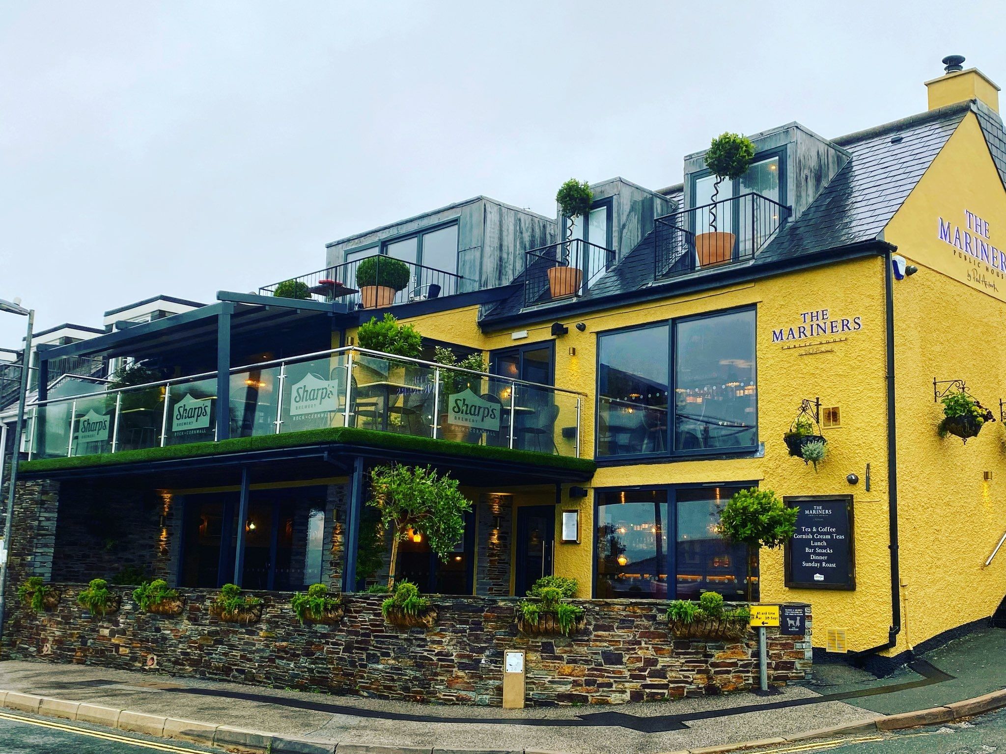 Exterior of The Mariners pub in Rock with yellow walls, glass terrace, and outdoor plants