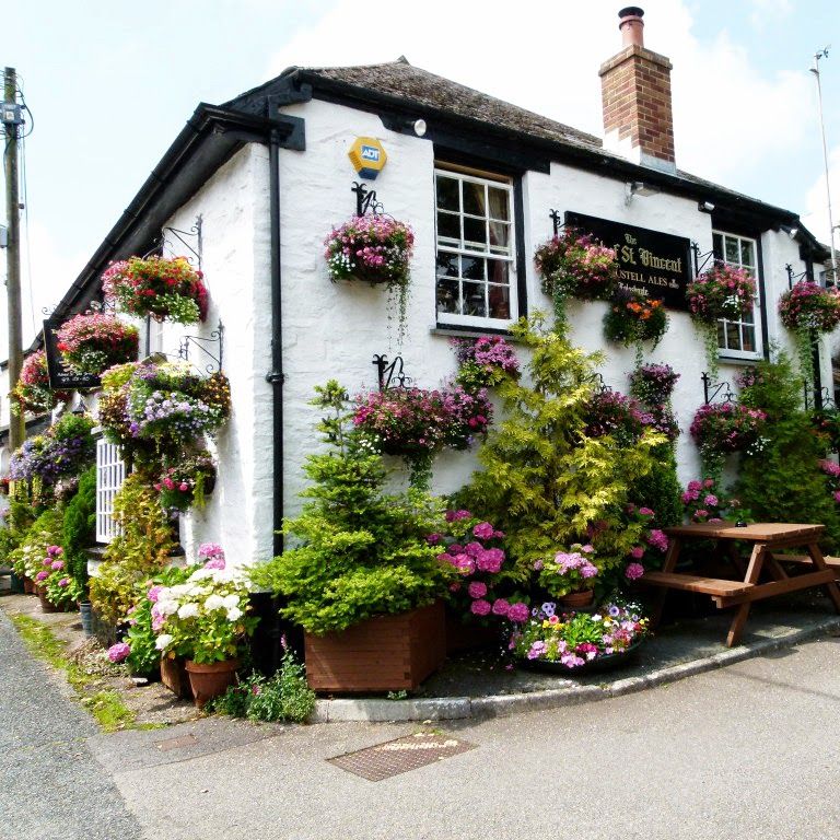 Charming white cottage pub covered in colorful hanging flower baskets and surrounded by greenery.