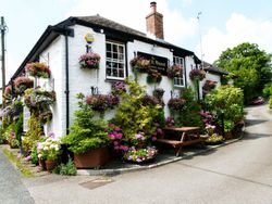 Charming white cottage pub covered in colorful hanging flower baskets and surrounded by greenery.