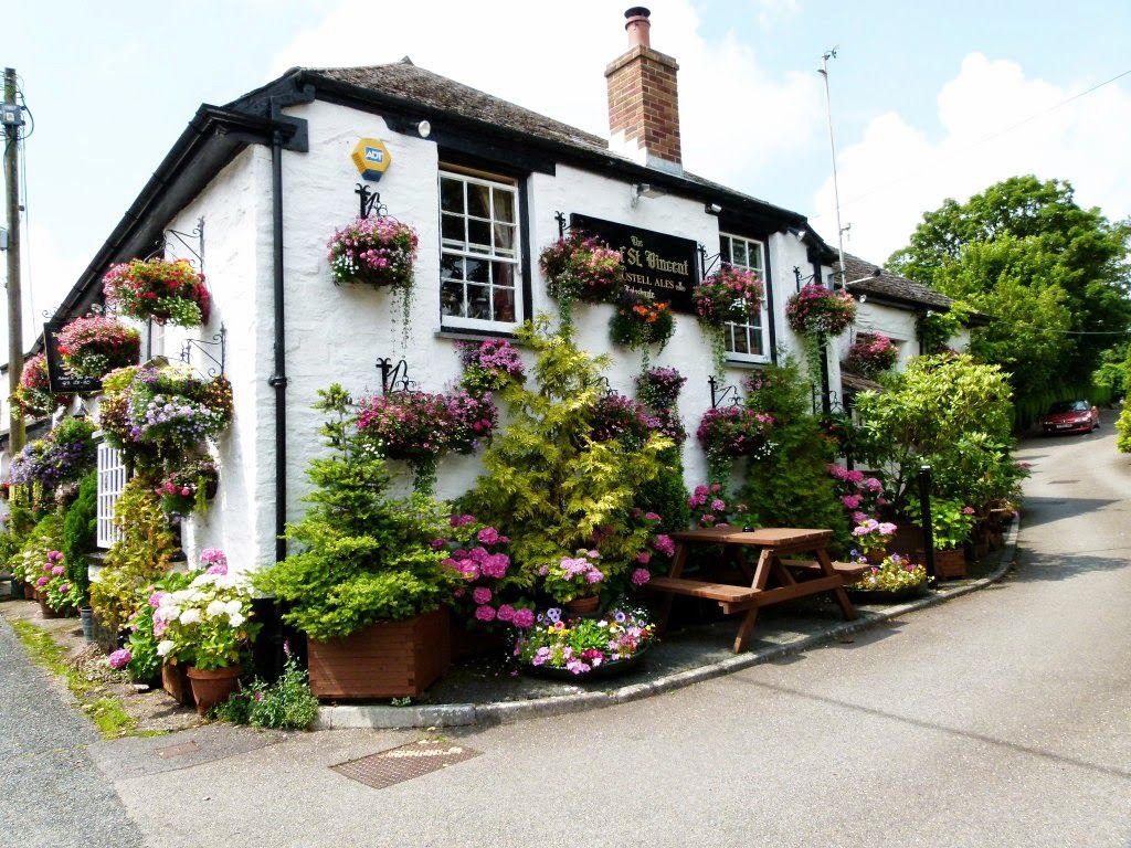 Charming white cottage pub covered in colorful hanging flower baskets and surrounded by greenery.