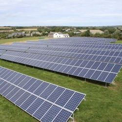 Solar panels installed on a grassy field with houses and countryside in the background