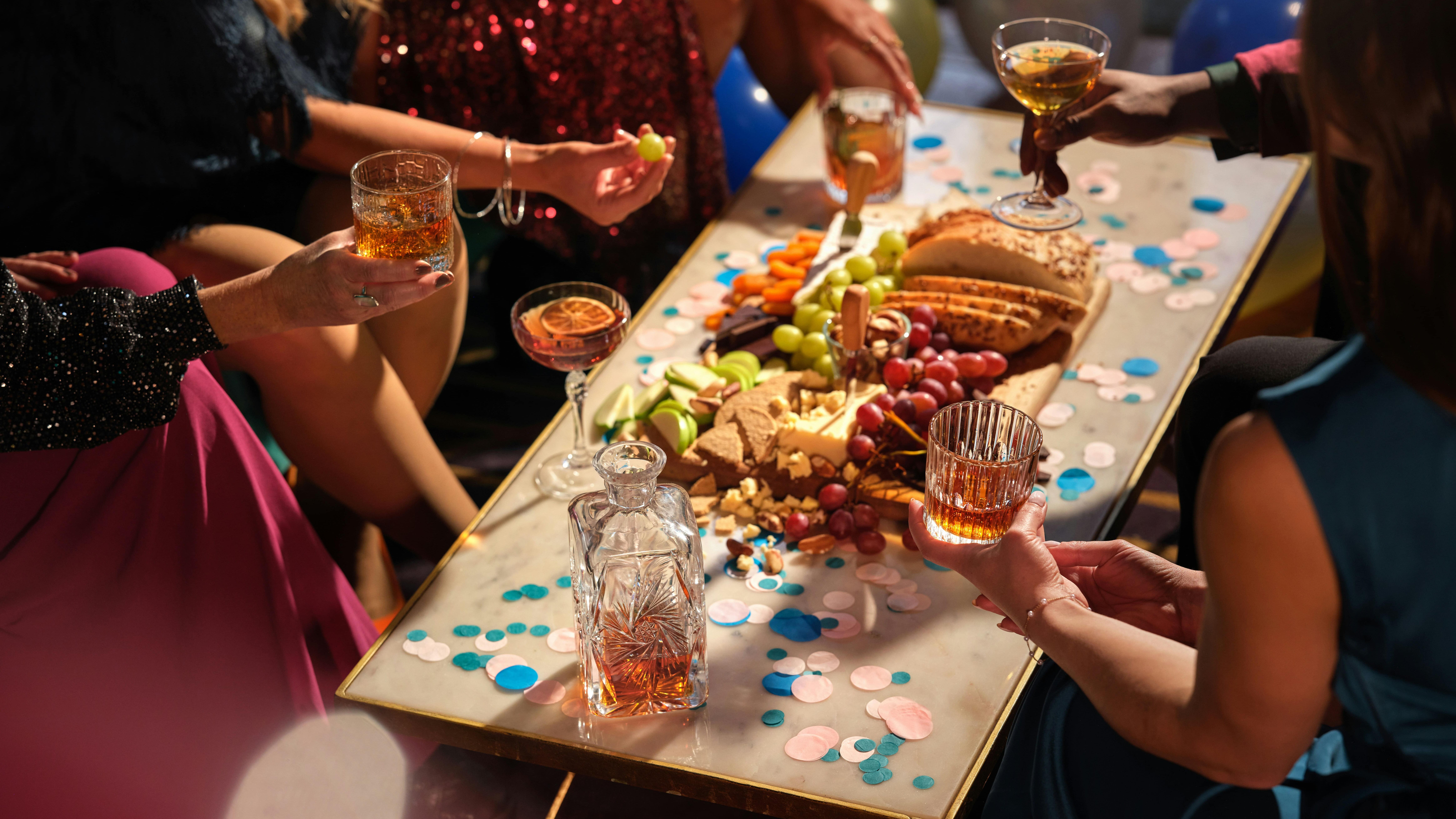 People enjoying drinks and snacks around a festive table with confetti and balloons.