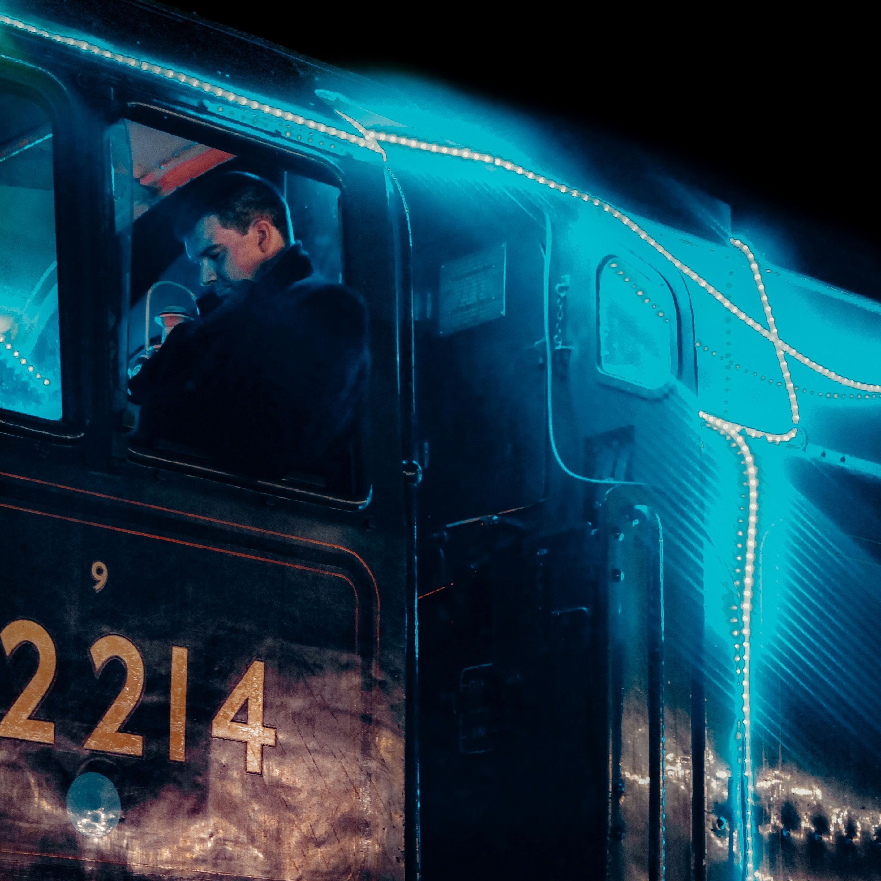 Train conductor inside the cab of a train engine decorated with blue neon lights at night