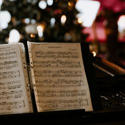 Open sheet music on a piano with a blurred Christmas tree in the background