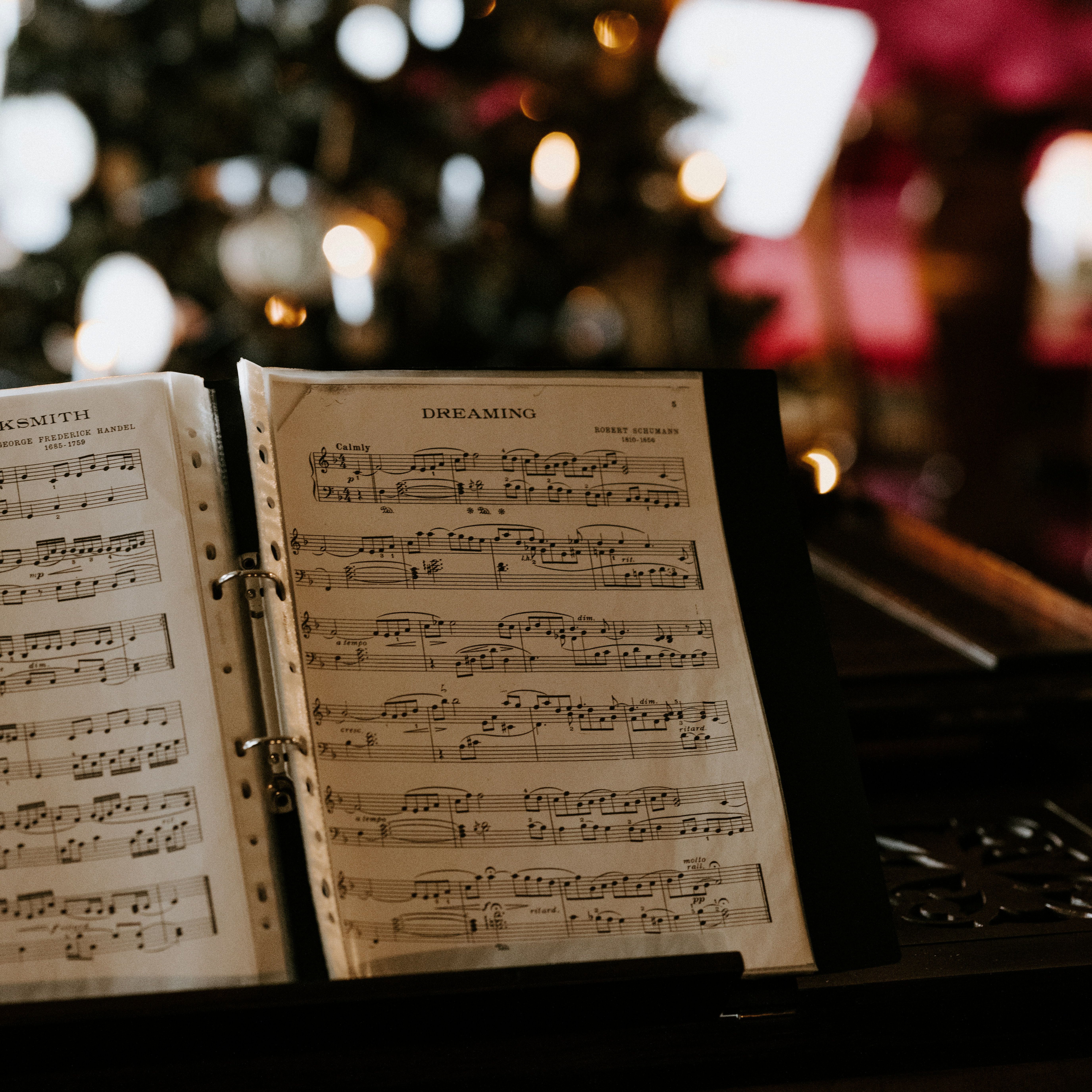 Open sheet music on a piano with a blurred Christmas tree in the background