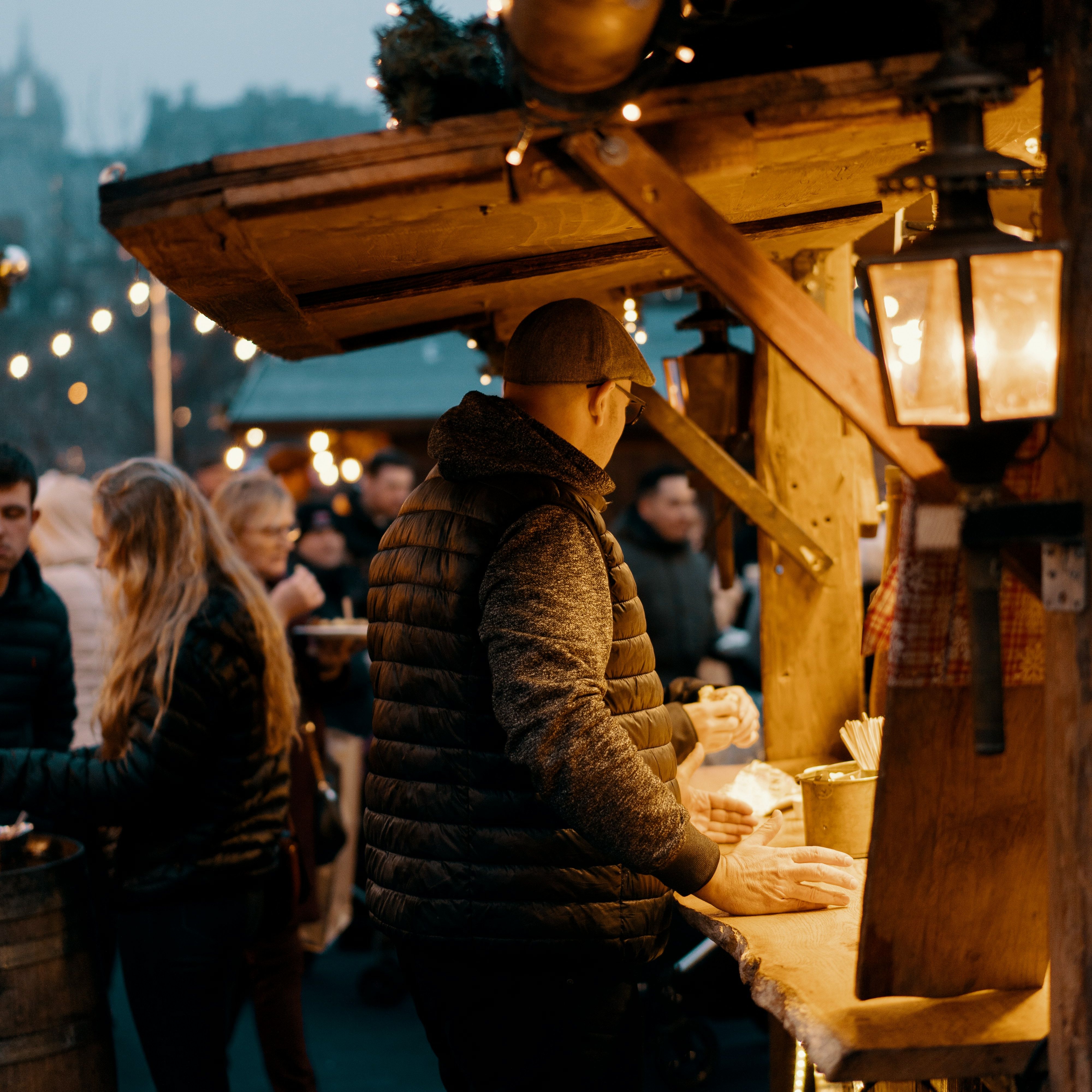 People ordering food at a cozy outdoor market stall with warm lights in the evening.