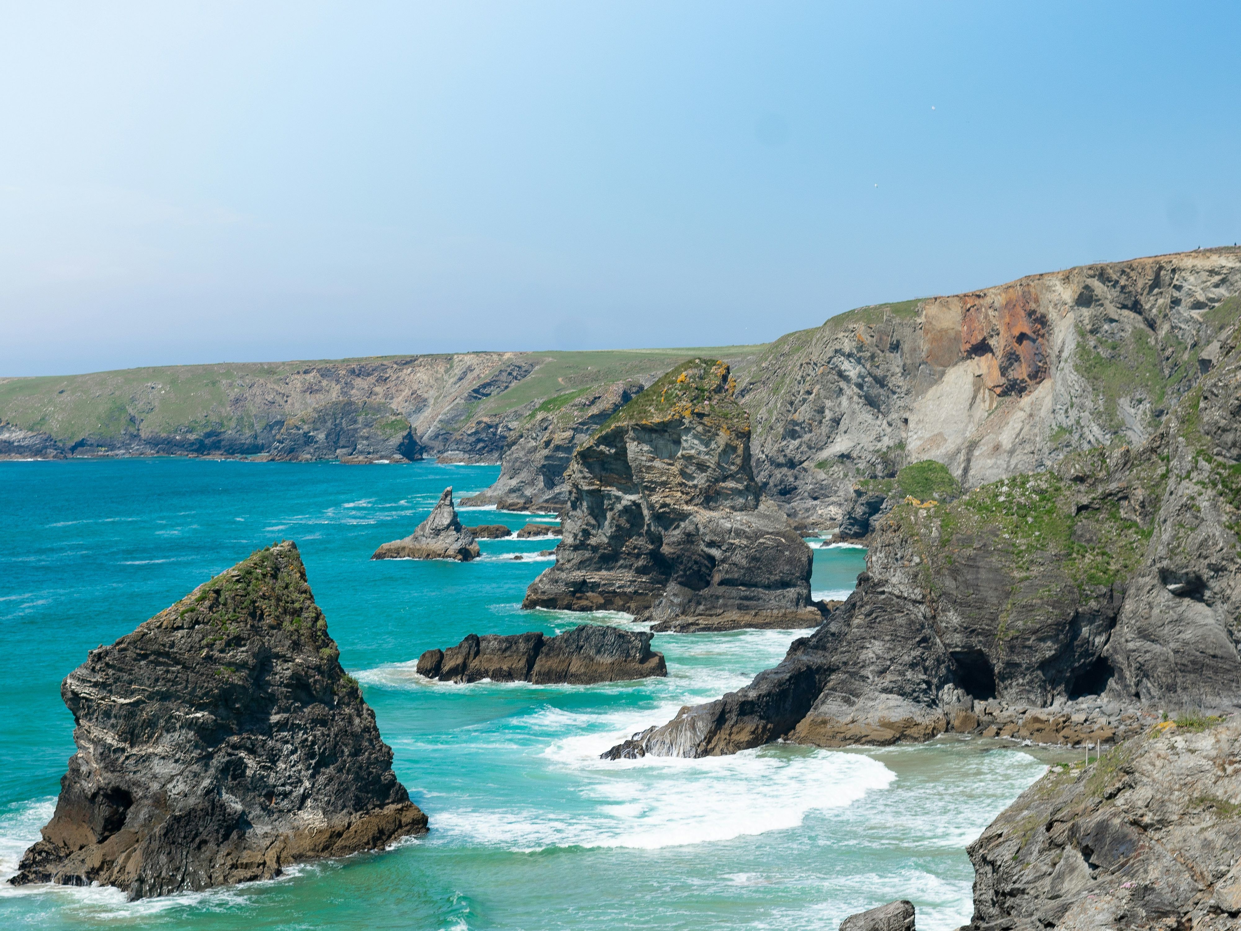 Rocky coastline with dramatic cliffs and turquoise sea under a clear blue sky.