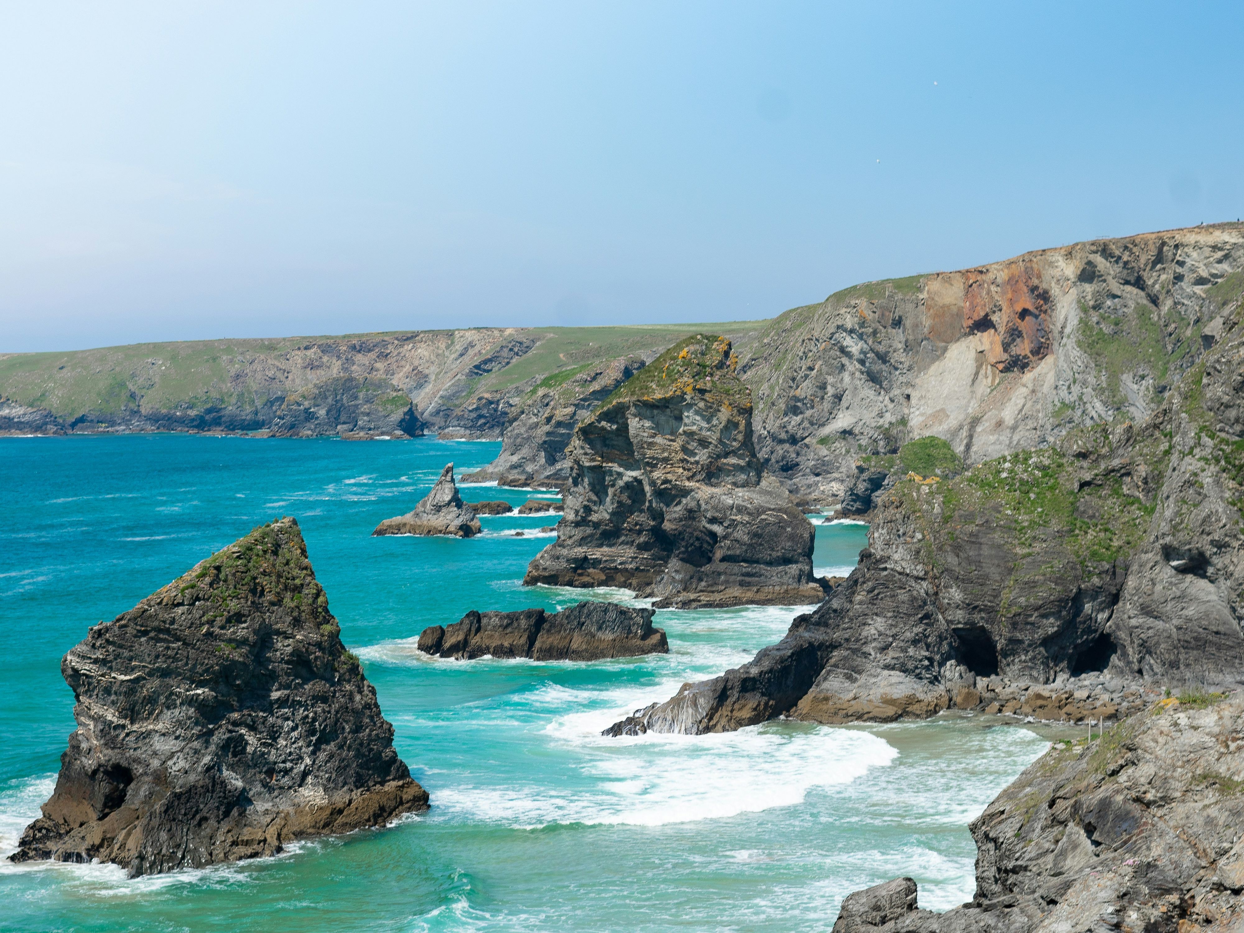 Rocky coastline with dramatic cliffs and turquoise sea under a clear blue sky.