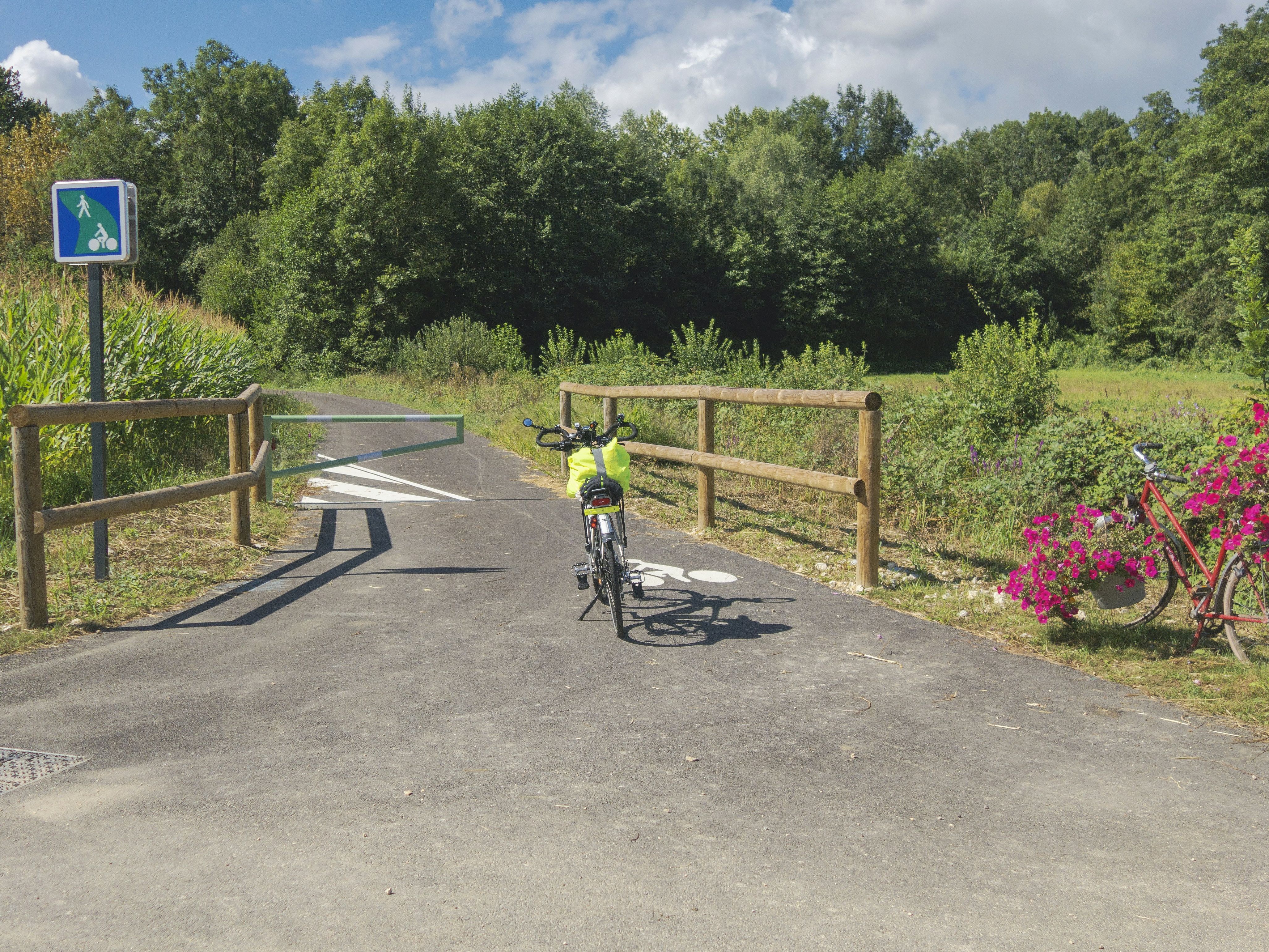 Bicycle parked on a rural bike path next to a flower-decorated bike and a walking and cycling sign