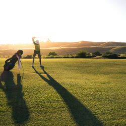Person preparing to swing a golf club on a golf course at sunset with long shadows cast on the grass