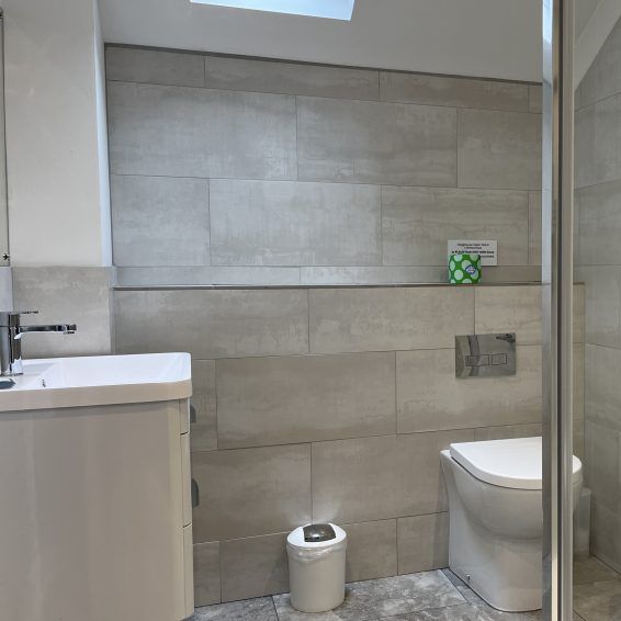 Modern bathroom with gray tiles, glass shower enclosure, toilet, and white vanity.