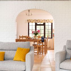 Modern living room with grey sofas and yellow cushions, looking through an archway to a dining table with flowers on it.