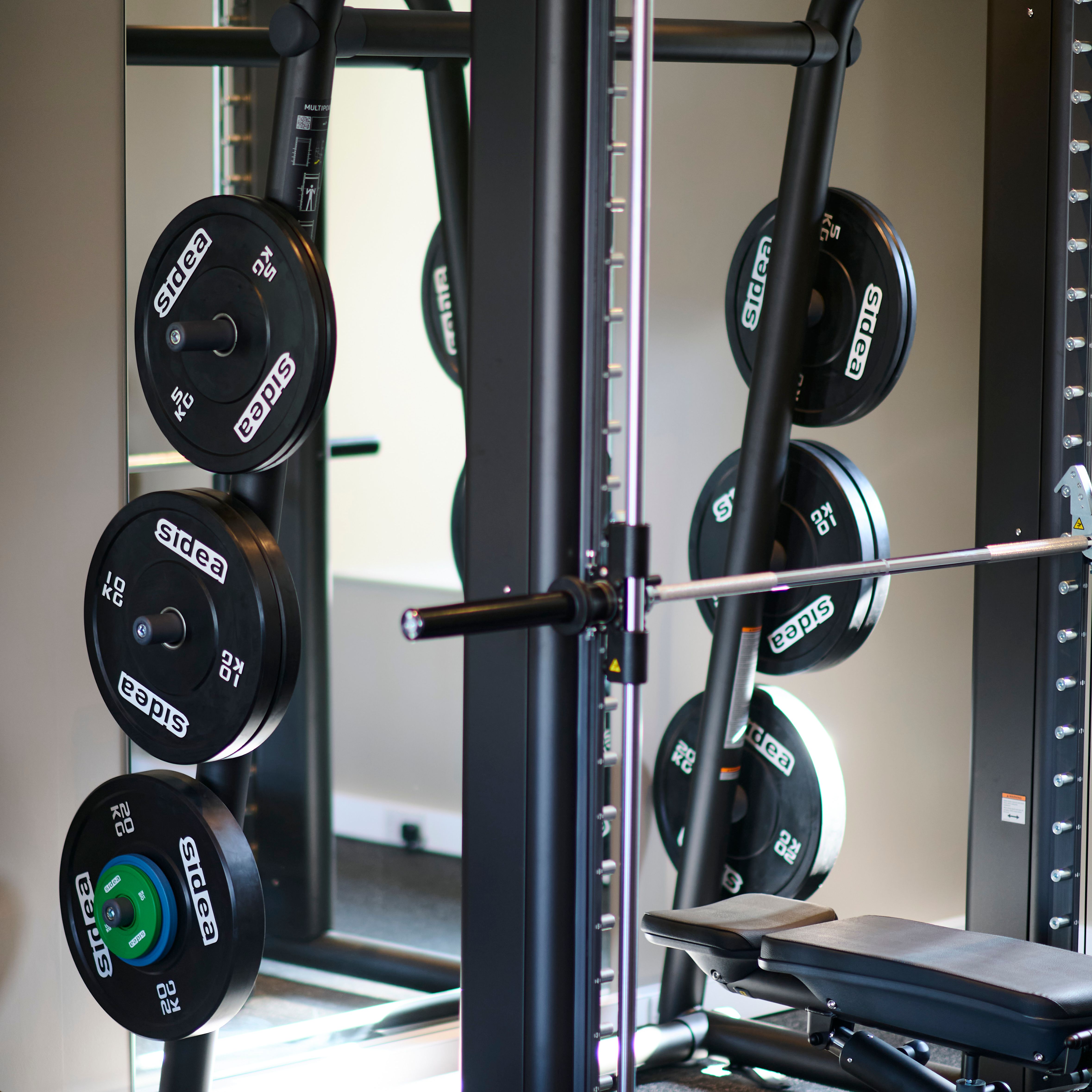 A close-up of a Smith machine in a gym, loaded with weight plates labeled 