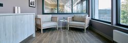 A cozy spa lounge area with two cushioned wooden chairs, a small table with a reed diffuser, large windows, and wood-style flooring.
