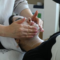 Woman receiving a facial treatment with cleanser being massaged into her skin by a therapist in a spa or skincare clinic setting.