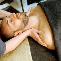 A man receiving a comforting massage lies on a massage bed, with the masseuse applying pressure to the collarbones.