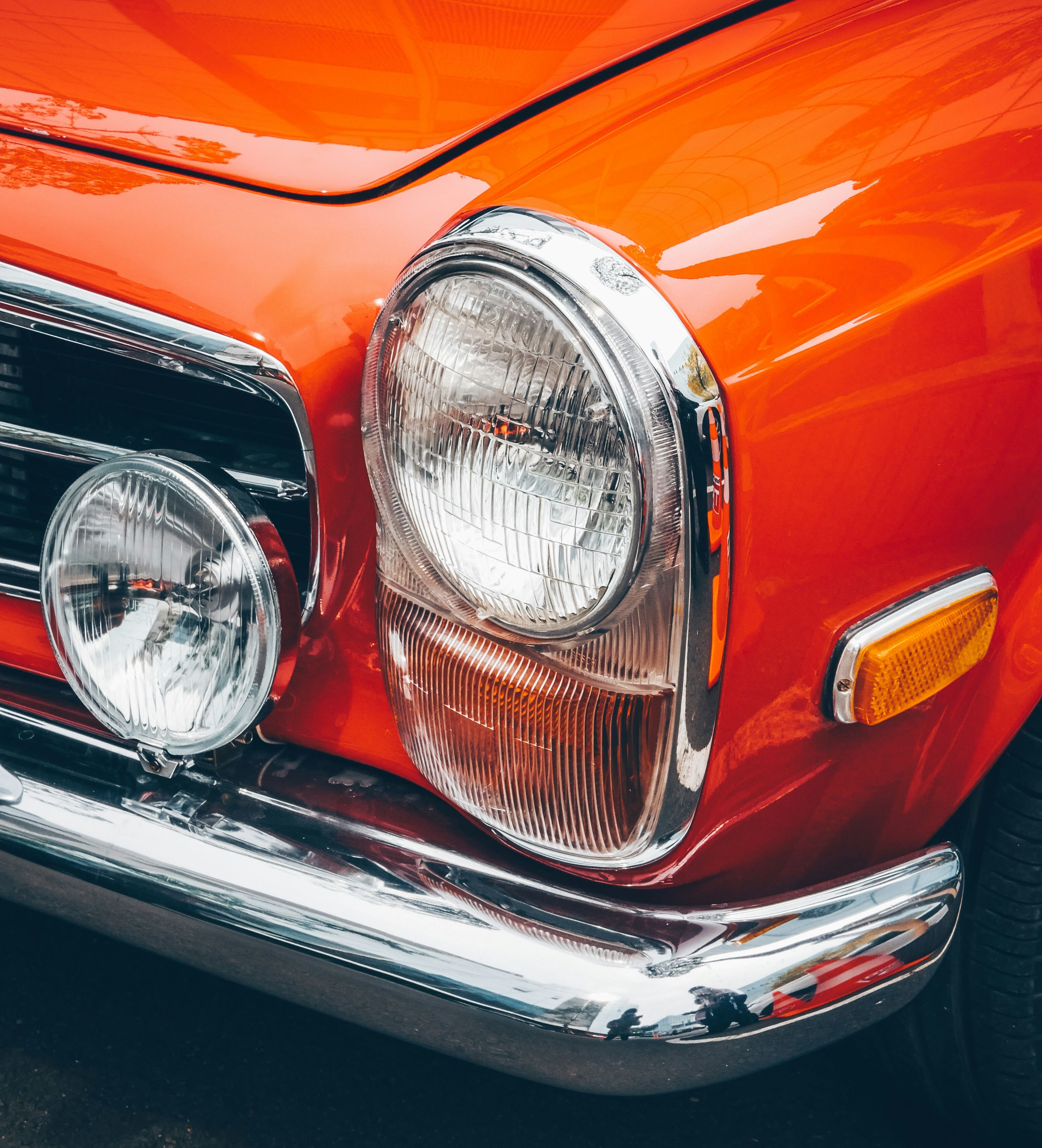 A close up shot of an orange vintage car, showcasing it's beautiful headlight features.