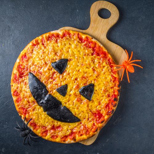 Pizza decorated like a jack-o'-lantern on a wooden board, with fake spiders