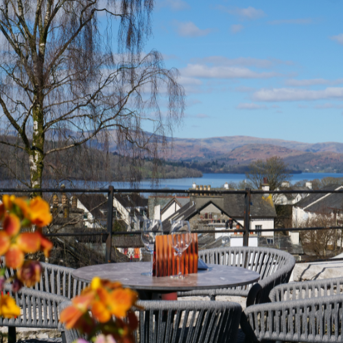 Outdoor patio table with glasses overlooking a scenic view of rooftops, trees, and distant hills under a blue sky.