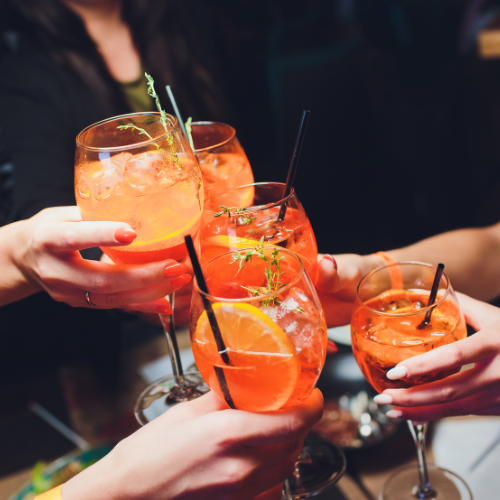 Group of people toasting with orange cocktails in wine glasses