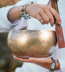 Person holding and playing a singing bowl with a wooden mallet