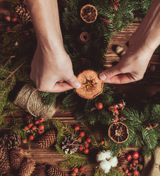Hands decorating a Christmas wreath with dried orange slices and natural materials
