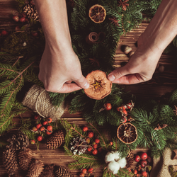 Hands decorating a Christmas wreath with dried orange slices and natural materials