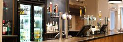 Modern bar with beer taps, illuminated pendant lights, and a fridge stocked with bottles.