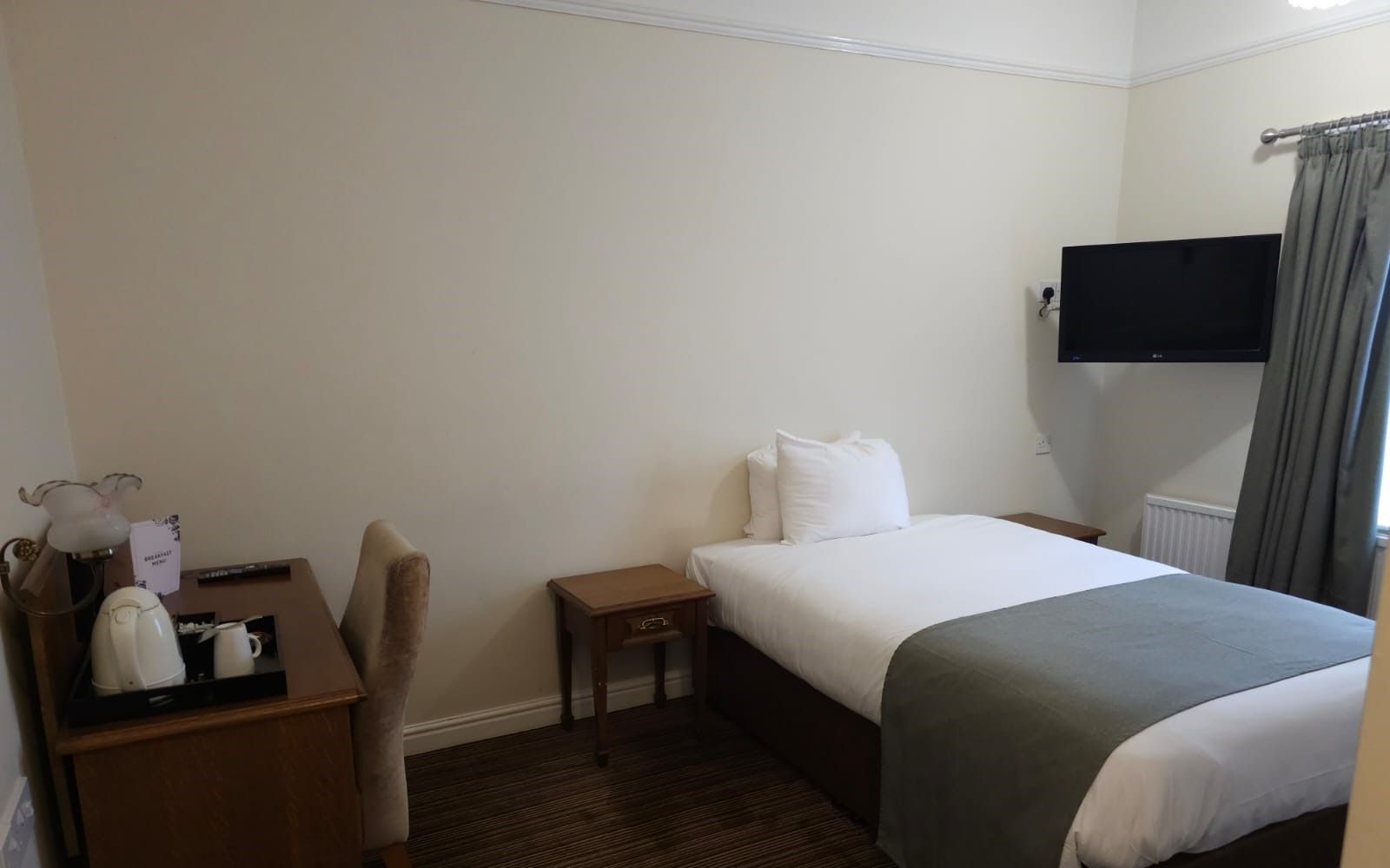 A tidy hotel room with a single bed, small desk, and television mounted on the wall.