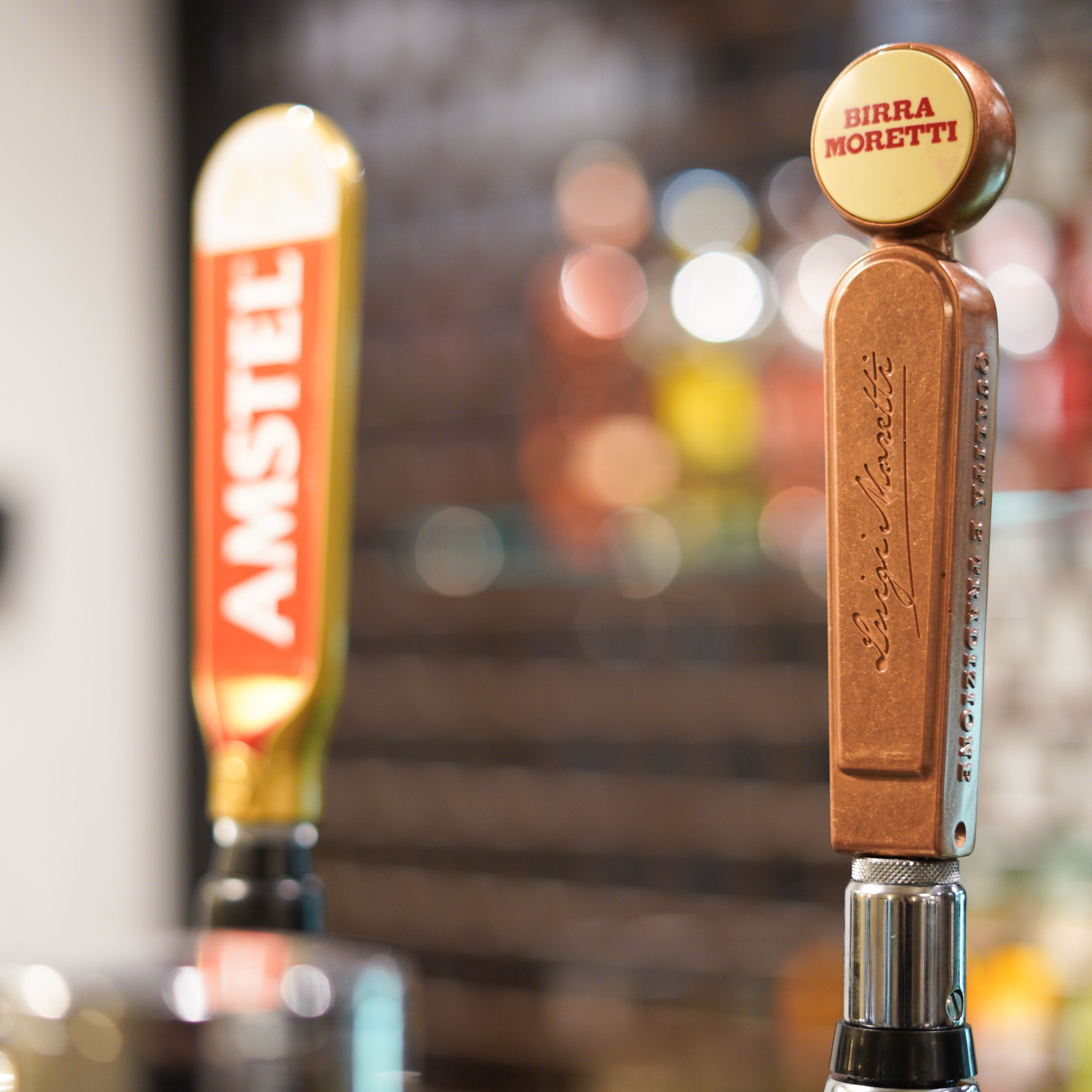 Close-up of two beer taps, one labeled Birra Moretti and the other Amstel.