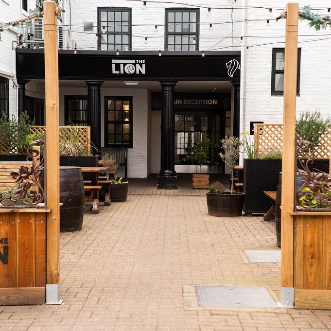 Alt tag: Main entrance of The Lion hotel with black pillars and sign, leading to the main reception
