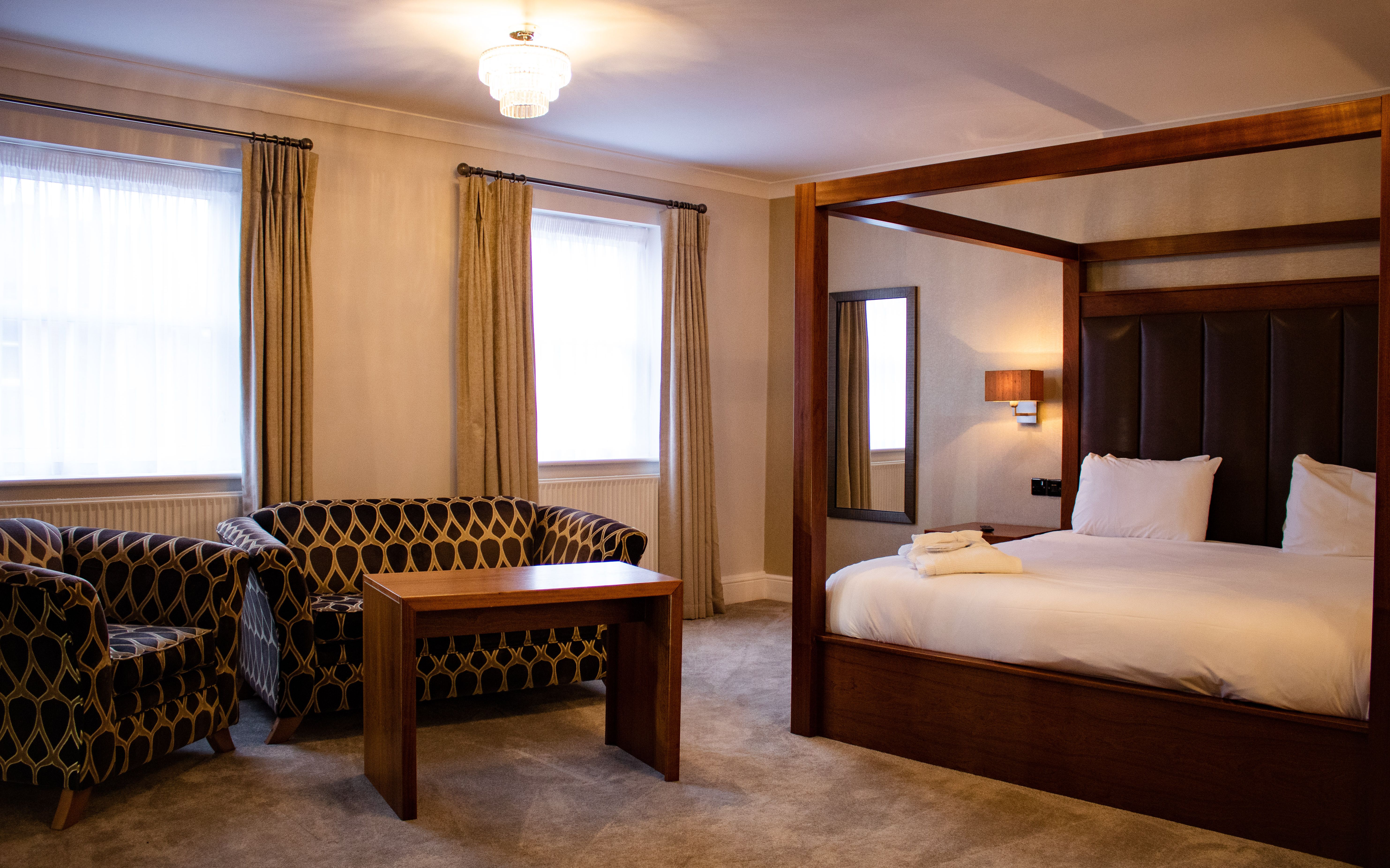 Spacious hotel suite with a large four-poster bed, contemporary seating area, and elegant furnishings.
