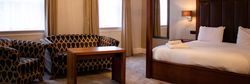 Spacious hotel suite with a large four-poster bed, contemporary seating area, and elegant furnishings.