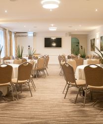 A conference room with round tables and beige chairs arranged neatly, decorated with potted plants.
