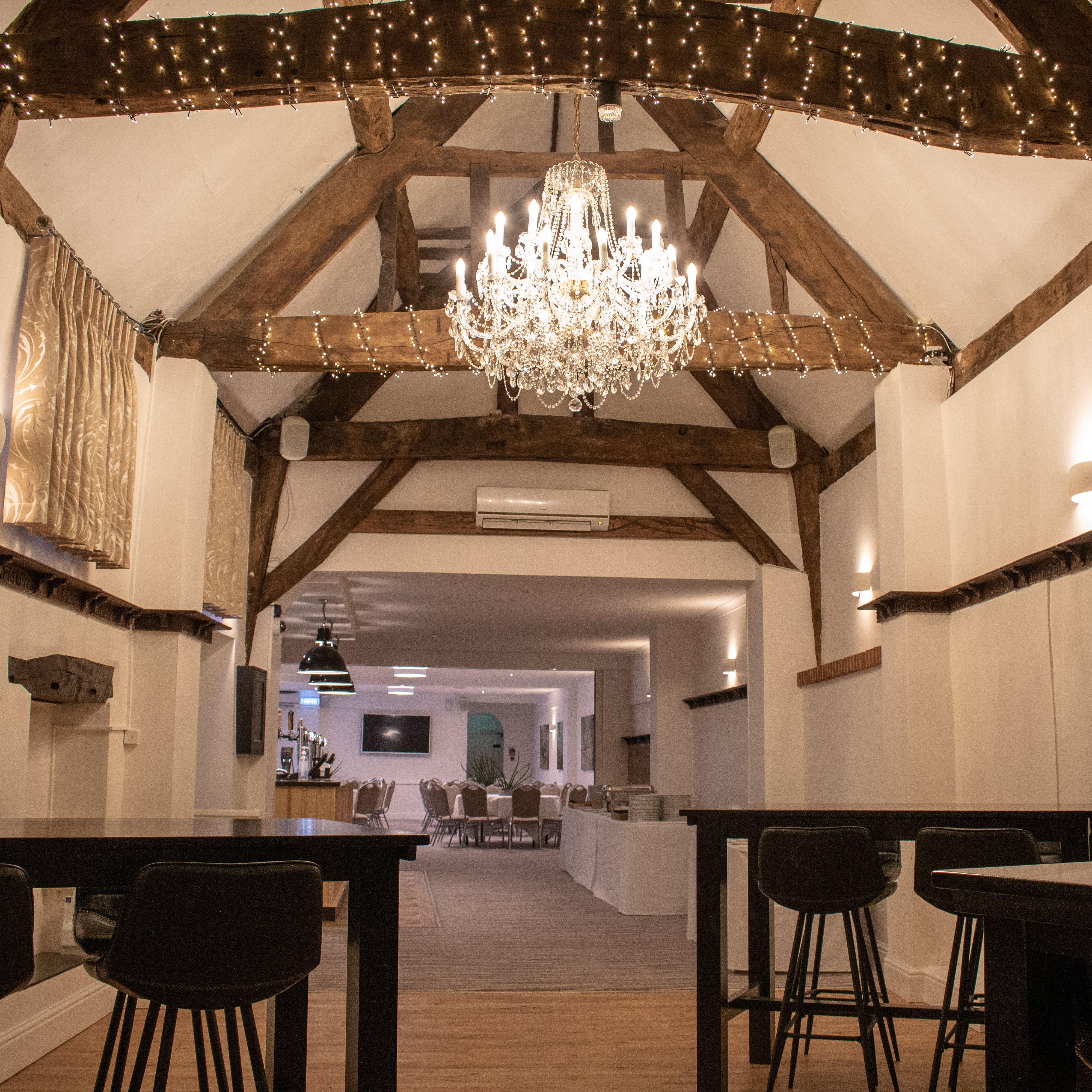 Rustic event space with exposed wooden beams, chandelier, and tables